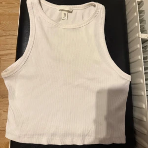 Vit ribbad linnetopp från H&M - Säljer en vit ribbad linnetopp från H&M i storlek M. Toppen är ärmlös med klassisk rund halsringning och croppad passform. Perfekt att matcha med jeans eller kjol för en enkel och fräsch look.