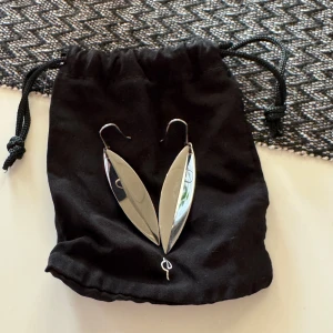 Silvriga örhängen från Edblad - Säljer ett par stilrena örhängen från Edblad i blankt silverfärgat material. De har en modern, avlång och böjd form som påminner om ett blad. Perfekta för dig som gillar minimalistisk och trendig design. Jag har aldrig använt dem men har inget kvitto