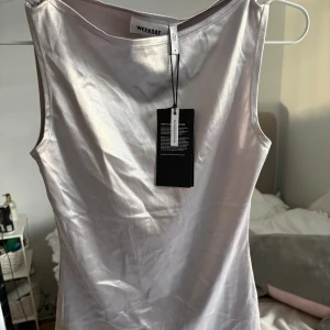 Silverfärgad linnetopp från Weekday - Säljer en snygg och glansig silverfärgad linnetopp från Weekday. Toppen är ärmlös och har en slät, stilren design i ett mjukt och följsamt material. Perfekt att styla med jeans eller kjol för en trendig look.