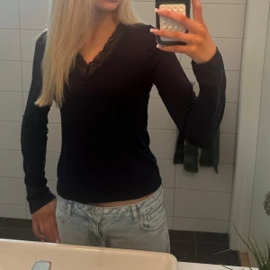 Svart långärmad blus med spets - Säljer en svart långärmad blus från Gina tricot med v-ringad hals och dekorativ spetskant. Toppen har en slim passform och är tillverkad i mjuk bomull som känns skön mot huden. Perfekt att styla med jeans eller kjol för en snygg look.