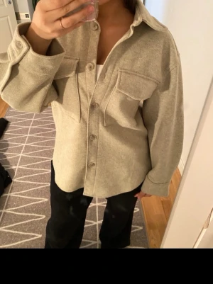 Beige overshirt med fickor - Snygg beige overshirt med stora bröstfickor och knappar hela vägen. Jackan har en loose passform och är tillverkad i ett mjukt material som känns skönt mot huden. Perfekt att slänga över en t-shirt för en chill look.