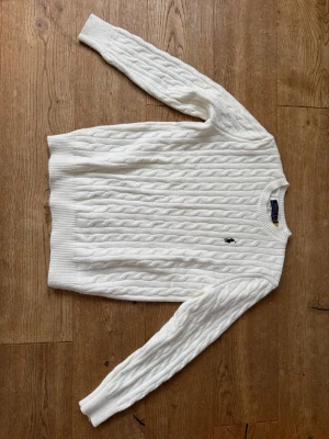 Vit kabelstickad tröja Polo Ralph Lauren - Kabelstickad vit tröja från Polo Ralph Lauren med klassisk broderad logga på bröstet. Tröjan har rund halsringning, ribbade muddar och är långärmad. Perfekt för dig som gillar tidlös och clean stil. Mycket fint skick och härligt mjukt material. Storlek L men passar även om man normalt använder M.