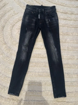 Svarta  jeans från Dsquared2 - Säljer ett par svarta jeans från Dsquared2 med slitningar och tvättade detaljer. Jeansen har klassisk femficksmodell, bälteshällor. Materialet är jeans med stretch för skön passform.