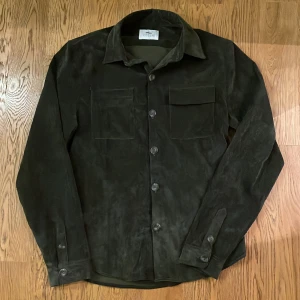 Svart -overshirt från Ciszere - Stilren grön overshirt från Ciszere. Skjortan har två bröstfickor med lock, klassisk krage och knäppning framtill. Perfekt för lager-på-lager och ger en cool vibe till din outfit.