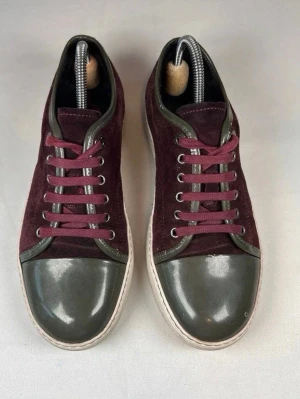 Lanvin captoe - Snygga sneakers från Lanvin i vinrött mocka med grå lackad tå och detaljer. Skorna har rund tå, snörning och vit platt sula. Perfekt för dig som gillar stilrena och unika sneakers med lyxig känsla.