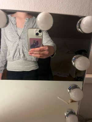 Ljusgrå kofta med knappar - Säljer en ljusgrå kofta med rund hals och långa ärmar. Koftan har en croppad passform och stängs med knappar framtill. Tillverkad i mjukt bomullsmaterial, perfekt att slänga över en topp för en chill look.