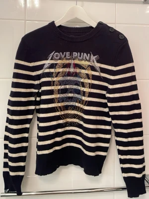 Randig tröja från Zadig & Voltaire - Snygg svart och vit randig tröja från Zadig & Voltaire med coolt 'LOVE PUNK'-tryck och döskalle framtill. Rund hals med två knappar på axeln och långa ärmar. Stickad i mjukt material.