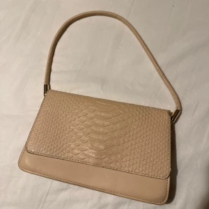 Beige axelväska med struktur - Säljer denna beiga axelväska med lite croco-material & lite detaljer i guld. I fint skick!💕