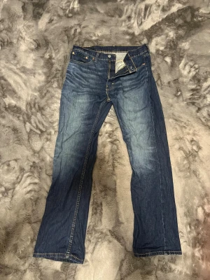 Levi's 527 blå jeans bootcut - Säljer ett par klassiska Levi's 527 jeans i blå tvätt med bootcut-snitt. Jeansen har fem fickor, gul kontrastsöm och Levi's patch bak i midjan. Materialet är slitstarkt denim i bomull och passformen är normal med lite vidare ben.             