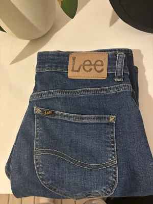 Blå jeans från Lee, storlek 14-15Y - Säljer ett par klassiska blå jeans från Lee med snygga kontrastsömmar och Lee-logga på bakfickan. Jeansen har normal passform och är tillverkade av 99% bomull och 1% elastan för lite stretch. Perfekt för dig som gillar tidlös denimstil.