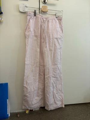 Ljusrosa linnebyxor med snörning - Säljer ett par ljusrosa linnebyxor med avslappnad passform och breda ben. Byxorna har elastisk midja med snörning, sidofickor fram och två fickor bak. Perfekta för chill dagar och sommarhäng.
