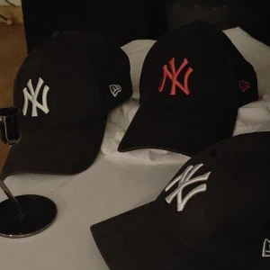 Svarta New Era kepsar med NY-logga - Säljer 3 svarta New Era keps med klassisk NY-logga framtill, finns med både vit och röd/ mörk rosa brodyr. Kepsarna är tillverkade i 100% bomull och har en böjd skärm. Perfekt för dig som vill ha en clean och sportig look. Jag anser de alla är unisex. Men den med röd/rosa logga står det woman in. Alla 3 är originella.  Med alla lappar och stämplar ! 