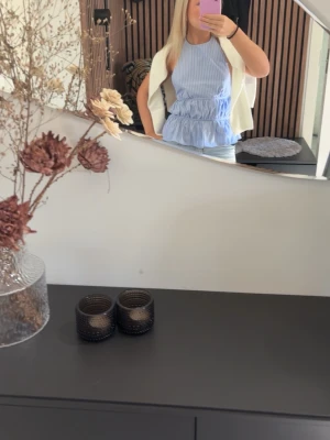 Blå- och vitrandig volangtopp Zara - Supersöt blå- och vitrandig topp från Zara med volangkant och halterneck. Toppen har en croppad passform och är ärmlös, perfekt till sommaren. Tillverkad i bomull för en luftig känsla och har justerbart band i nacken.