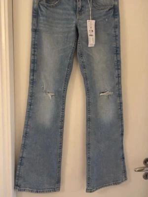 Lågmidu bootcut jeans  - Blå Lågmidjade bootcut jeans från Gina tricot med hål på knäna, knappar på bakfickorna, aldrig andvända 💘