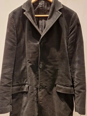 Svart kavaj från Rice, storlek 48 - Superfin herrock, enkelknäppt, från Rice. Storlek 48. Yttertyg i blandning av kammad bommul och ull. Smala slag och två sidofickor med lock. Innerfordret är lite fransigt i ärmslut och kan behöva en lagning av den som vill. Pris 1000 kr (nypris 4995)