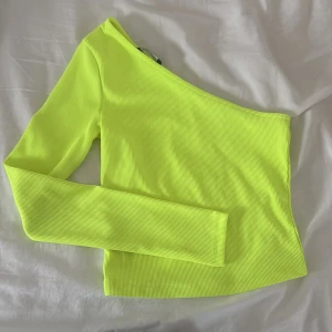 Neongul oneshoulder topp - Säljer en ribbad neongul topp med oneshoulder-design och lång ärm från Bershka.