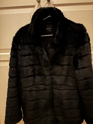 Svart pälsjacka från mq, strl 40 - Säljer en svart pälsjacka från mq i storlek 40. Jackan har en fluffig och mjuk känsla med horisontella ränder och klassisk krage. Perfekt för dig som vill ha en varm och snygg look under kyliga dagar. Jackan är långärmad och har en loose passform.