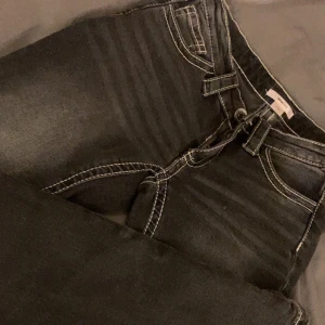Låg midjade svart/grå jeans - Svarta jeans från Gina Tricot med vita kontrastsömmar och snygga detaljer på bakfickorna. Andvända fåtal gånger, skulle gissa på 2/3 gånger, så har inga spår av andvändning. Mycket fina låg midjade jeans med bootcut och är i strl 34