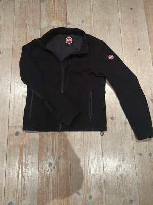Svart vindjacka från Colmar - Svart vindjacka från Colmar med stilren design och diskret logga på ärmen. Jackan har hel dragkedja framtill, två sidofickor med dragkedja och hög krage. Materialet är syntet och ger en sportig känsla. Perfekt för dig som gillar clean och funktionell stil.