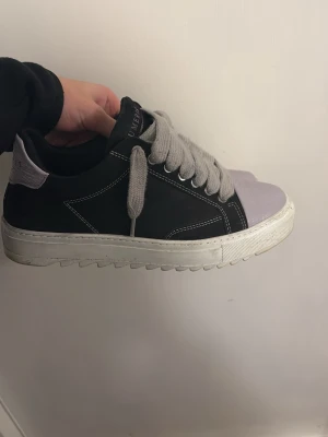 Svarta sneakers med lila tå från Numeris - Säljer ett par chunky sneakers från Numeris med svart ovandel dom är lite små och dem finns inte längre och köpa, ljuslila tåparti och breda grå snören. Skorna har vit sula med räfflad kant och kontrastsömmar. Perfekta för dig som vill sticka ut med en unik färgkombo och cool design. Box o allt finns 