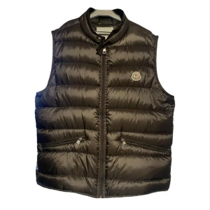 Brun Moncler Väst - Säljer denna stilrena väst från Moncler (Äkta) eftersom jag planerar att köpa nått nytt. Västen är sparsamt använd och i gott skick. Den enda skadan är en repa på framsidan (Sista bilden) och därav sänkt pris. Västen passar till det mesta och är perfekt för vår sommar och höst. Vid funderingar är det bara att höra av sig!