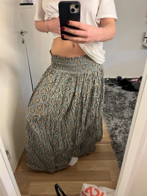 Zara långkjol  - Säljer denna snygga långkjol med ett härligt mönster i vitt och grönt. Kjolen har bred resår i midjan och är gjord i ett tunt, mjukt bomullstyg som känns luftigt. Perfekt för dig som gillar boho-vibbar och vill ha något bekvämt och snyggt.