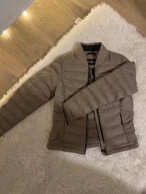 Beige pufferjacka från Sail Racing XS - Säljer en beige pufferjacka från Sail Racing i storlek XS. Jackan har quiltad design, lång ärm och dragkedja framtill. Materialet är syntet och jackan har en stilren look med svart detalj på kragen. Perfekt för kyliga dagar. Fleece i jackfickorna. Jackan är så gott som ny, använd endast vid finare tillfällen