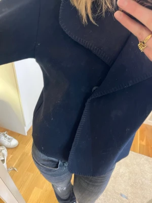 Mörkblå kappa från Gina Tricot - Säljer en mörkblå kappa från Gina Tricot med bred krage och raka ärmar. Jackan har en stilren design, stängs med knappar framtill och har detaljer längst kanterna. Perfekt för dig som gillar en enkel men snygg look. 💖