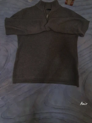 Brun ribbad stickad tröja med half zip - Säljer en brun stickad tröja med ribbad struktur och half zip framtill. Tröjan har lång ärm och en hög krage som ger extra värme. Perfekt för dig som gillar en enkel men snygg look under kyliga dagar.