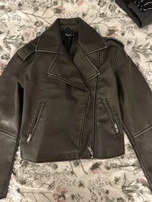 Svart skinnjacka från Gina tricot  - Snygg svart skinnjacka med klassisk bikerstil från Gina tricot . Den är helt helt ny och jag har prislappen kvar Jackan har stora slag, två sneda dragkedjefickor och en assymetrisk dragkedja framtill. Materialet är skinnimitation och insidan är fodrad med svart tyg. Perfekt för dig som gillar edgy stil.