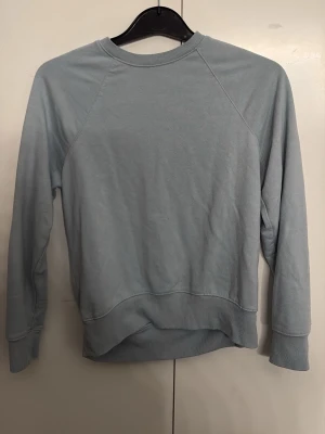 Ljusblå sweatshirt från H&M, XS - En enkel och stilren ljusblå sweatshirt från H&M i storlek XS. Tröjan har rund hals, långa ärmar och ribbade muddar vid ärmslut och nederkant. Perfekt för chill dagar och passar till jeans eller mjukisbyxor.