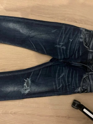 Replay jeans blå, storlek 32 - Säljer ett par snygga Replay jeans i mörkblå tvätt med slitningar och trasiga detaljer på benen. Modellen har klassiska fem fickor, smal passform och normal midja. Materialet är jeans med stretch för extra komfort. Perfekt för dig som gillar en cool och avslappnad stil.