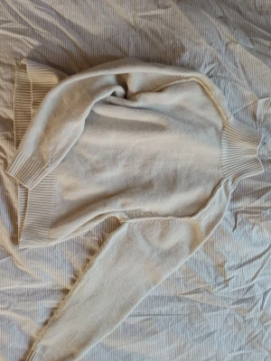 Beige stickad polotröja - Mysig beige stickad polotröja med bred ribbad mudd vid ärmslut, nederkant och hals. Tröjan har en relaxed passform och är perfekt för kyliga dagar. Enkel och stilren design som funkar till allt. Aldrig använd endast testad och tvättad då jag inte tyckte beiget passade mig.