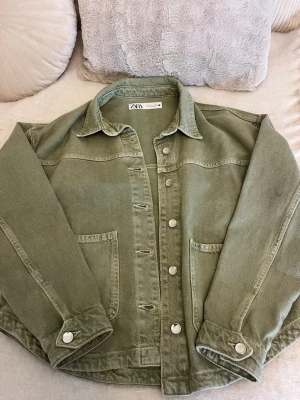 Olivgrön jeansjacka från Zara - Olivgrön jeansjacka från Zara med stora fickor framtill och silverfärgade knappar. Jackan har två fläckar en på varje arm, men är säker på att det går att få bort. Annars är den i väldigt bra skick💖