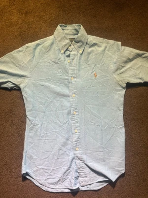 Blå slim fit skjorta från Polo Ralph Lauren - Säljer en ljusblå stretch oxford-skjorta från Polo Ralph Lauren i slim fit. Skjortan har klassisk krage, knappar hela vägen och den ikoniska broderade loggan på bröstet. Perfekt för dig som gillar stilrena och snygga plagg. Finns små difekter skriv om ni vill ha bild!