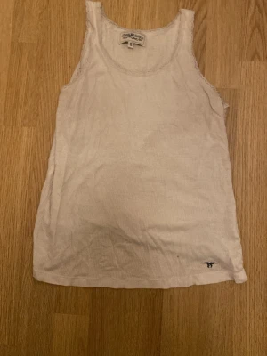 Vit ribbad linnetopp från Napapijri - Säljer en vit ribbad linnetopp från Napapijri med rund halsringning och ärmlös design. Toppen har diskreta ränder och ett litet broderat logomärke nere vid kanten. Perfekt för varma dagar och enkel att matcha med jeans eller shorts.