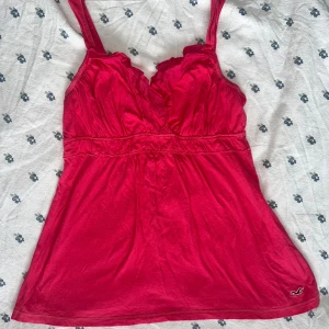 Rosa babydoll linnetopp från Hollister - Snygg rosa babydoll linnetopp från Hollister i 100% bomull. Toppen har breda axelband, v-ringad hals med volangdetaljer och markerad midja. Perfekt för varma dagar och enkel att matcha med jeans eller kjol. Vintage storlek L den passa till S och M. 