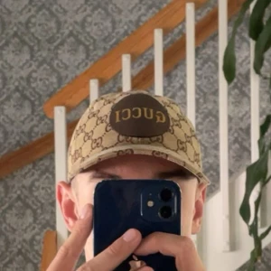 Beige keps från Gucci med GG-mönster - Säljer en beige keps från Gucci med klassiskt GG-monogram över hela kepsen och en brun patch framtill med Gucci-logga. Justerbar rem baktill i samma mönster. Snygg och tidlös accessoar som lyfter vilken outfit som helst.  PM för mer information!