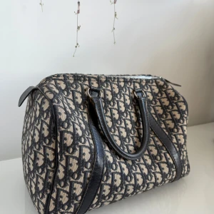 Christian Dior monogram handväska - Säljer en ikonisk handväska från Christian Dior med klassiskt monogrammönster i svart och beige. Väskan har svarta skinnhandtag och detaljer, dragkedja upptill och rymlig form.  Älskar denna!!! .köpte den från collectorscage.se 