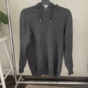 Kashmir hoodie  - Mysig mörkgrå hoodie från Roge med huva och dragsko.Perfekt för kyliga dagar när du vill vara både bekväm och snygg. Enkel och stilren design som funkar till det mesta. Har en liten defekt uppe vid kragen men syns ej när man har på sig den.