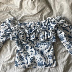 Blommig offshoulder blus med volang - Superfin blus med offshoulder och volangdetaljer, vit botten med blått blommigt mönster.Skriv ifall intresserad💞💞