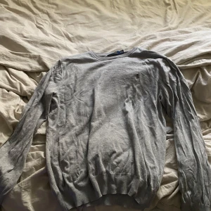 Grå tröja från Polo Ralph Lauren - Säljer en stilren grå tröja från Polo Ralph Lauren i slim fit-modell. Tröjan är tillverkad i mjuk pima bomull och har rund hals samt diskret broderad logga på bröstet. Perfekt för dig som gillar klassisk och enkel stil