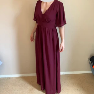 Vinröd långklänning med v-ringning - Vinröd långklänning med V-ringning. Knytning i midjan bak samt osynlig dragkedja i sidan