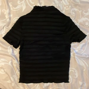 Svart ribbad topp från HM - Svart kortärmad topp från HM i storlek S. Helt oanvänd. Tröjan har en ribbad struktur med horisontella ränder och en lätt stretchig känsla. Perfekt att styla med jeans eller kjol för en clean look. Priset går att diskutera 