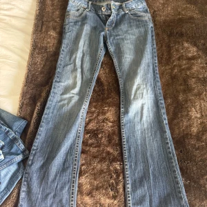 Ljusblå bootcut jeans med låg midja - Säljer ett par ljusblå jeans med bootcut-modell och låg midja. Jeansen har klassisk femficksdesign, knapp- och dragkedjestängning samt snygga slitningar framtill. Perfekta för en avslappnad och trendig look.