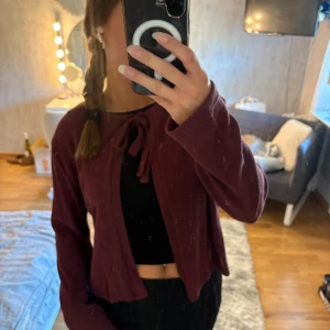 Vinröd kofta med knyt från 157 - Säljer en vinröd kofta från 157 i storlek M. Koftan har ett snyggt knyt framtill vid halsen och är gjord i mjukt stickat material. Modellen är croppad och har långa ärmar, perfekt att slänga över en topp för en chill look. Fin färg inför hösten som passar perfekt till ett par jeans.