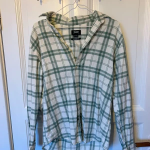 Grönvit rutig skjorta Pull&Bear - Säljer en grön och vit rutig skjorta från Pull&Bear i relaxed fit. Skjortan har långa ärmar, klassisk krage och knäppning framtill. Perfekt för en chill och avslappnad stil. Materialet är mjukt och skönt.