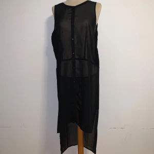 Svart genomskinlig långklänning från Size & Needle - Svart transparent långklänning från Size & Needle i storlek S. Klänningen är ärmlös med knappar framtill och har en öppen rygg. Klänningen har en längre bakdel.