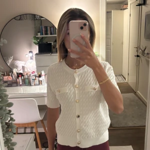 Vit kabelstickad topp - Vit stickad topp med guldknappar och fick detaljer. Super mysigt och stretchigt material. Står ingen storlek i den men skulle säga att det är en XS/S. Hör av dig om du har några frågor! 🫶🏼💕