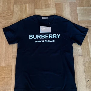 Svart Burberry t-shirt med tryck - Svart t-shirt från Burberry med klassiskt vitt tryck 'BURBERRY LONDON ENGLAND' på bröstet                        !!!!!Kan sänka priset vid snabbafärr!!!!!